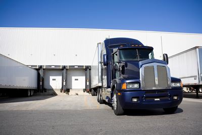 A blue transport truck is docked at a warehouse